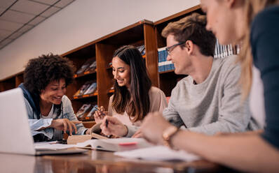 Junge Leute sitzen am Tisch und lesen Nachschlagewerke für Studiennotizen. Gruppe junger Studenten, die eine Aufgabe in der Bibliothek erledigen. - JLPSF01183