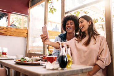 Fröhliche Frau, die ein Selfie mit ihrem Freund in einem Café macht. Ein Paar, das sich mit seinem Smartphone in einem Café amüsiert - JLPSF01197