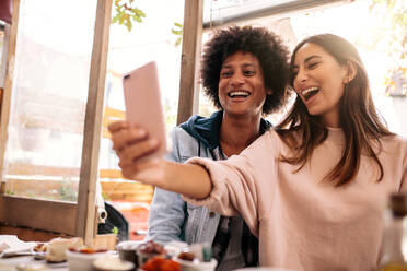 Junges Paar sitzt im Café und nimmt Selfie mit Smartphone. Schöne Frau nimmt Selbstporträt mit ihrem Freund im Restaurant. - JLPSF01199