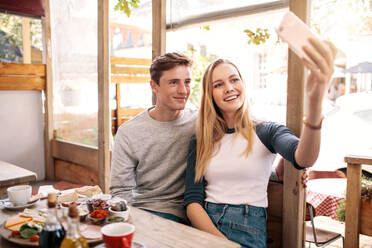 Ein Paar, das sich mit dem Handy in einem Café fotografiert. Ein stilvolles junges Paar, das mit dem Smartphone Erinnerungen festhält. - JLPSF01201