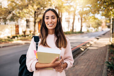 Schöne junge Frau mit Buch auf dem Weg zum College. Junge Studentin mit Buch auf dem Campus. - JLPSF01204