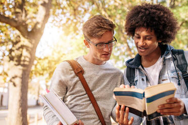 Männliche Universitätsstudenten mit Buch auf der Straße. Junge Studenten, die draußen gemeinsam ein Buch lesen. - JLPSF01222