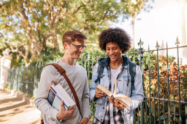 Junge männliche Studenten mit Buch, die auf der Straße spazieren gehen, Universitätsstudenten, die ein Buch betrachten. - JLPSF01223