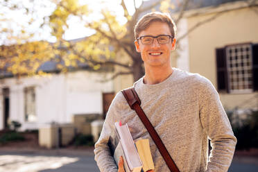 Glücklicher männlicher Student im Freien mit Büchern. Junger Universitätsstudent mit Büchern auf dem Campus. - JLPSF01225