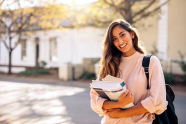 Beautiful young woman with backpack and books outdoors. College student carrying lots of books in college campus. - JLPSF01226