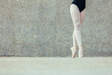 Closeup shot of legs of a female ballet dancer standing on her toes wearing pointe shoes. Ballet dancer practicing dance moves. - JLPSF01227