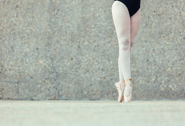 Closeup shot of legs of a female ballet dancer standing on her toes wearing pointe shoes. Ballet dancer practicing dance moves. - JLPSF01228