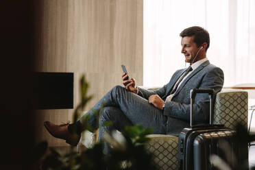 Geschäftsmann, der einen Videoanruf per Mobiltelefon tätigt, während er auf seinen Flug wartet. Geschäftsmann in der Flughafen-Lounge, der eine Videokonferenz mit seinem Smartphone abhält. - JLPSF01240