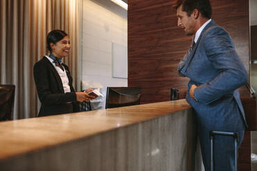 Geschäftsmann checkt an der Hotelrezeption ein. Weibliche Empfangsdame an der Rezeption im Gespräch mit einem Gast im Hotel. - JLPSF01252