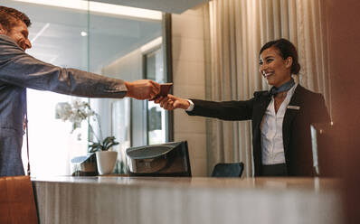 Businessman passes his passport to a smiling receptionist behind the hotel counter. Check-in process in luxurious hotel. - JLPSF01255