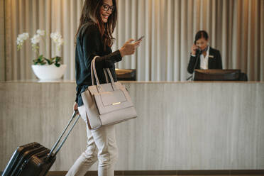 Eine Frau benutzt ein Mobiltelefon und zieht ihren Koffer in einer Hotellobby. Eine Geschäftsreisende geht durch einen Hotelflur. - JLPSF01260