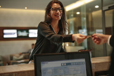 Asiatische Geschäftsfrau, die an der Rezeption die Schlüsselkarte für ein Hotelzimmer entgegennimmt. Weiblicher Gast, der am Check-in-Schalter die Schlüsselkarte für sein Zimmer entgegennimmt. - JLPSF01261