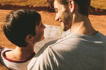 Rückansicht eines Paares, das sich anschaut und lächelt, während es eine Landkarte in der Hand hält. Mann und Frau halten eine Karte zur Navigation auf einer Autoreise. - JLPSF01286