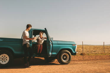 Couple enjoying a road trip in the country side in their car. Woman sitting in the car with the door open while the man stands out holding a navigation map. - JLPSF01288