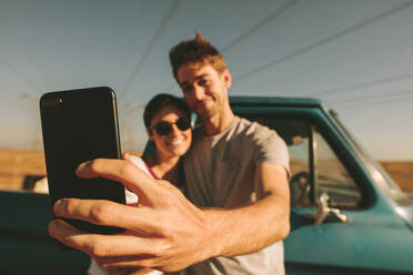 Ein Paar genießt einen Roadtrip auf dem Lande und stellt sich für ein Selfie auf, während es sich gegenseitig festhält. - JLPSF01289