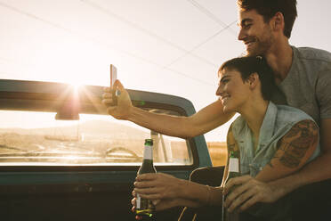 Nahaufnahme eines Paares, das ein Selfie mit dem Handy macht, während es auf der Rückbank seines Pick-ups sitzt. Ein fröhliches Paar sitzt auf der Rückbank seines Pick-ups und genießt die Fahrt auf dem Land. - JLPSF01299