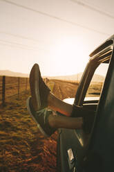 Close up of legs of a relaxing woman hanging out from car on a highway in country side. Legs hanging out from car. - JLPSF01302