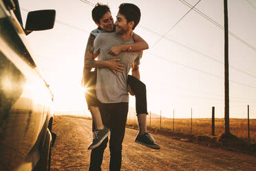 Woman piggy riding on a man outdoors in country side. Man carrying a woman on his back while on a road trip. - JLPSF01308