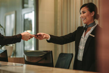 Smiling receptionist behind the hotel counter attending female guest. Concierge giving the documents to hotel guest. - JLPSF01313