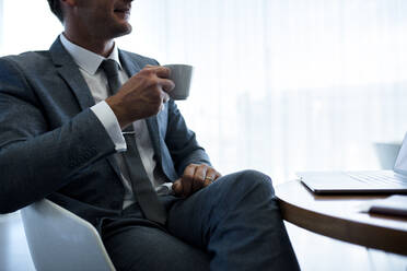 Abgeschnittene Aufnahme eines Geschäftsmannes, der in der Büro-Lobby sitzt und Kaffee trinkt. Ein Unternehmer trinkt Kaffee im Büro. - JLPSF01327