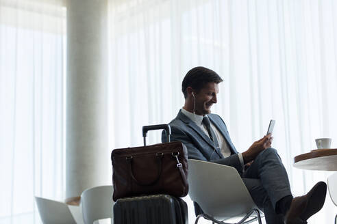 Geschäftsmann sitzt in der Flughafen-Lounge mit Handy. Geschäftsreisender macht einen Videoanruf, während er auf seinen Flug wartet. - JLPSF01331