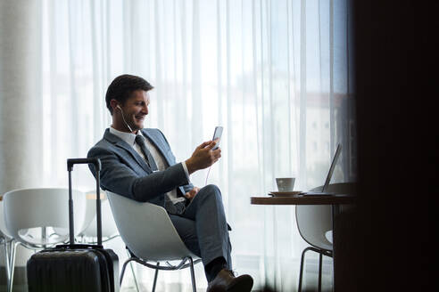 Geschäftsmann auf Geschäftsreise, der in der Flughafenlounge auf seinen Flug wartet und einen Videoanruf von seinem Mobiltelefon aus tätigt. - JLPSF01332