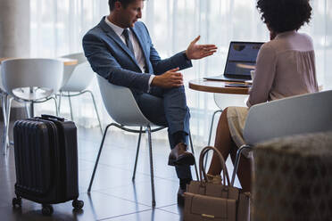 Geschäftsmann zeigt Frau etwas, während er in der Flughafen-Lounge sitzt. Geschäftsleute arbeiten am Laptop, während sie auf ihren Flug warten. - JLPSF01335