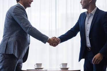 Two business men shaking hands with each other after a deal. Businesspeople shaking hands making a necessary agreement during a meeting. - JLPSF01347