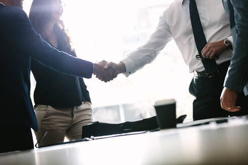 Partners concluding deal and shaking hands in the presence of team members. Businessmen shaking hands in board room and finishing up a meeting. - JLPSF01356