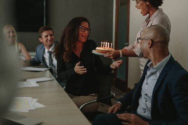 Afrikanische Frau, die einer weiblichen Führungskraft im Konferenzraum einen Geburtstagskuchen schenkt. Arbeiter feiern den Geburtstag eines Kollegen im Büro während einer Besprechung. - JLPSF01364