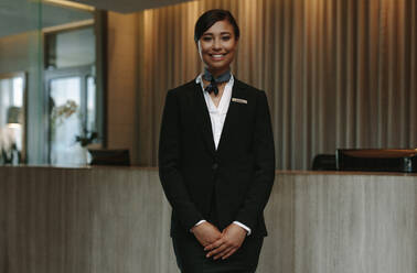 Glücklich lächelnde weibliche Rezeptionistin in einem Hotel. Schöne Concierge in Uniform wartet darauf, die Gäste zu begrüßen. - JLPSF01371