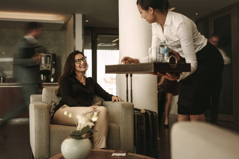 Das Personal der Business Lounge serviert einer weiblichen Reisenden im Wartebereich Kaffee. Eine Geschäftsfrau wartet in der Abflughalle des Flughafens. - JLPSF01382