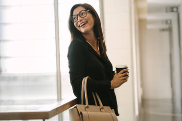 Lächelnde Geschäftsfrau im Büro stehend mit einer Tasse Kaffee. Weibliche Führungskraft im Büro stehend während der Pause. - JLPSF01390