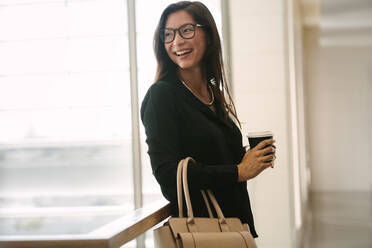 Asian business woman standing in office holding a cup of coffee. Female executive during break in office. - JLPSF01392