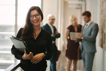 Porträt einer lächelnden Geschäftsfrau mit Kollegen, die im Hintergrund stehen und die Arbeit besprechen. Asiatische Managerin mit Mitarbeitern im Hintergrund. - JLPSF01393
