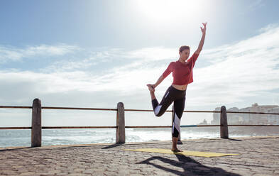 Aktive junge Frau macht Dehnungsübungen im Freien. Fitness-Frau übt in Yoga-Pose auf der Straße am Meer. - JLPSF01403