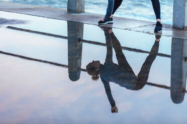 Trainierende Frau Reflexion in Pfütze von Wasser auf der Straße. Fitness weiblich tun Stretching Workout auf nassen Straße entlang des Meeres. - JLPSF01414