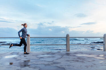 Außenaufnahme einer jungen Frau, die am Strand entlang joggt. Eine Läuferin läuft im Freien an der Strandpromenade. - JLPSF01417