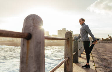 Frau Läufer tun Stretching-Übungen an der Strandpromenade. Fitness weiblich stehend durch ein Geländer für die Durchführung von Warm-up-Strecken. - JLPSF01425