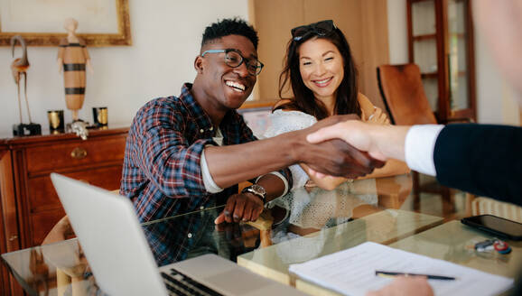 Happy property owners shaking hands with real estate broker after a deal. Young couple handshaking real estate agent after signing contract. - JLPSF01452