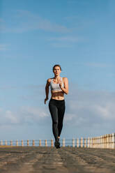 Full length shot of fit young woman running on the seaside promenade. Female runner working out in morning. - JLPSF01464