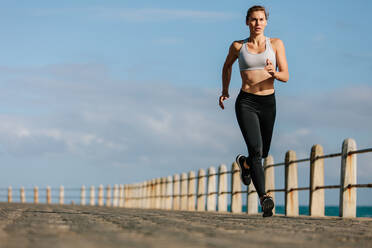 Fitte Sportlerin beim Laufen auf einer Straße am Meer. Läuferin beim Training auf einer Strandpromenade. - JLPSF01470