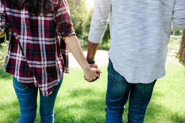 Rückansicht eines verliebten Paares, das sich im Freien an den Händen hält, bei einer Verabredung im Park. Aufnahme von hinten von einem Mann und einer Frau, die zusammen draußen spazieren gehen. - JLPSF01474