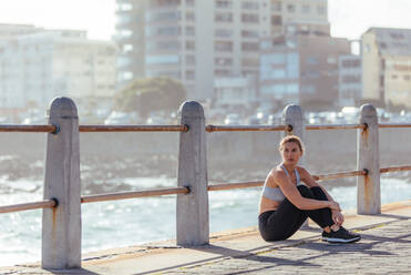 Läuferin, die nach einem Fitnesstraining im Freien am Meer eine Pause einlegt. Frau, die sich nach einem Morgenlauf auf der Straße am Meer entspannt. - JLPSF01475