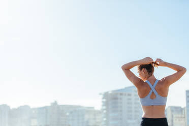 Rückansicht einer fitten Sportlerin, die sich vor dem Training die Haare bindet. Junge Frau, die sich auf das Training vorbereitet. - JLPSF01476