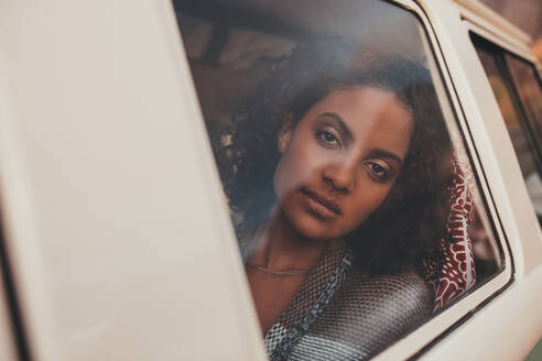 Nachdenkliche afrikanische Frau, die im Van sitzt und aus dem Fenster schaut. Nahaufnahme einer Frau, die aus dem Fenster eines Vans schaut. - JLPSF01483
