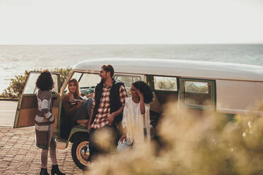 Friends hanging out together by a van. Group of man and women standing by an old minivan on roadside, taking rest during the road trip. - JLPSF01526