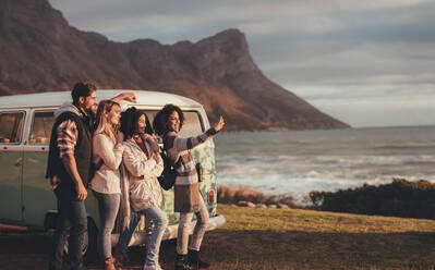 Freunde auf Autoreise nehmen Selbstporträt mit Handy durch den Minivan. Gruppe von Mann und Frauen zusammen ein Selfie machen, während in der Nähe der van stehen. - JLPSF01535