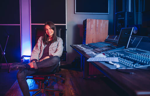 Glückliche junge Frau in einem Tonstudio, eine Musikkomponistin sitzt am Mischpult. - JLPSF01541