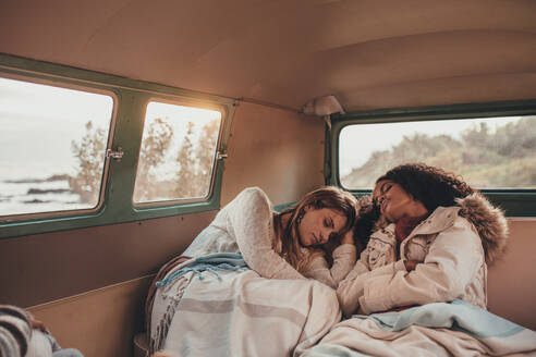 Zwei Freundinnen auf einer Autoreise schlafen im Van. Freundinnen schlafen auf dem Rücksitz eines Autos während der Reise. - JLPSF01544